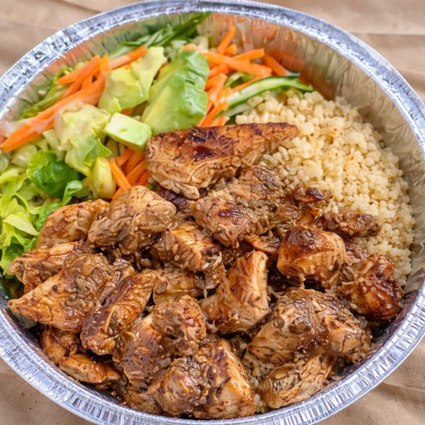 Chicken and quinoa bowl with fresh salad, carrots, and avocado in a foil container.