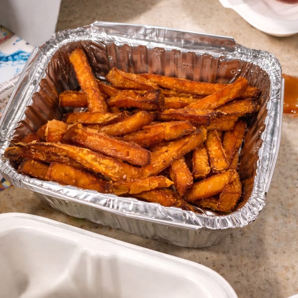 Sweet potato fries in a silver foil takeout container on a light brown counter.